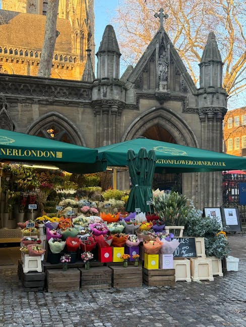 An outdoor flower stall situated in front of a historic stone church with gothic architectural features such as pointed arches and spires. The stand, covered by a green canopy with the website 'bighto