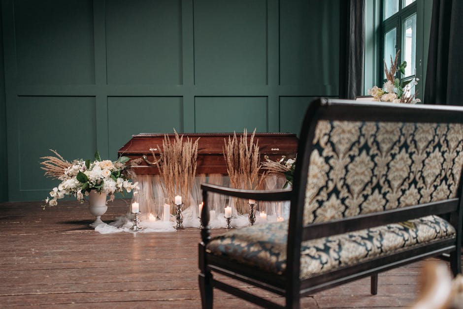 A floral arrangement featuring soft pastel-colored flowers, including white roses, blush peonies, and light greenery, is displayed on a wooden table alongside a vintage-style urn filled with similar b